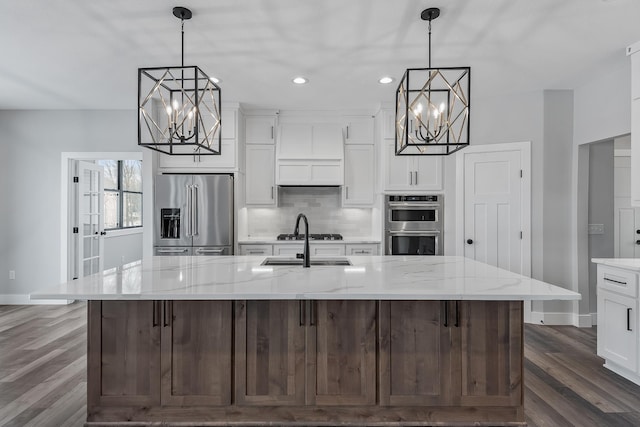 kitchen with pendant lighting, a large island with sink, appliances with stainless steel finishes, dark hardwood / wood-style flooring, and light stone counters