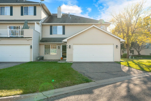 view of property featuring a front yard, a balcony, a garage, and cooling unit