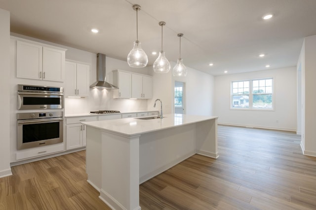 kitchen featuring a kitchen island with sink, white cabinets, wall chimney range hood, and light wood-type flooring