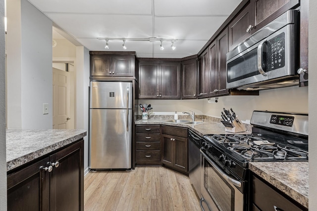 kitchen with rail lighting, sink, dark brown cabinetry, stainless steel appliances, and light hardwood / wood-style flooring