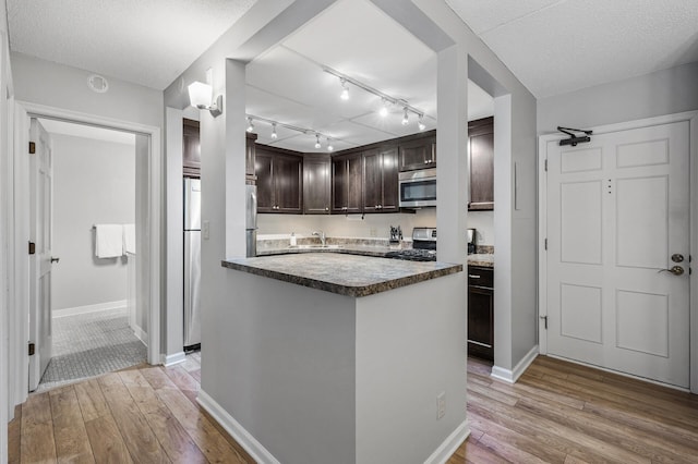 kitchen featuring dark brown cabinetry, appliances with stainless steel finishes, a textured ceiling, and light wood-type flooring