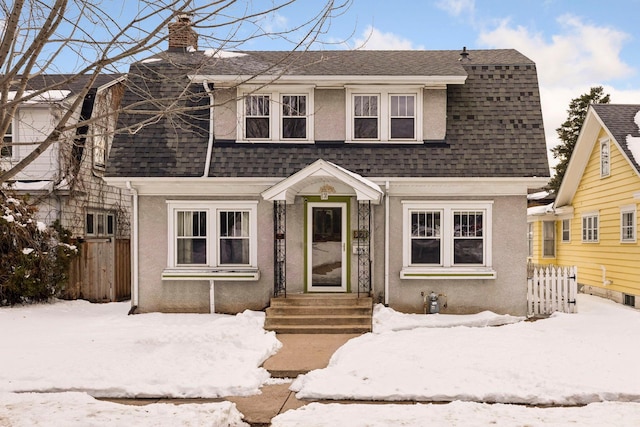 dutch colonial featuring a shingled roof, fence, and stucco siding