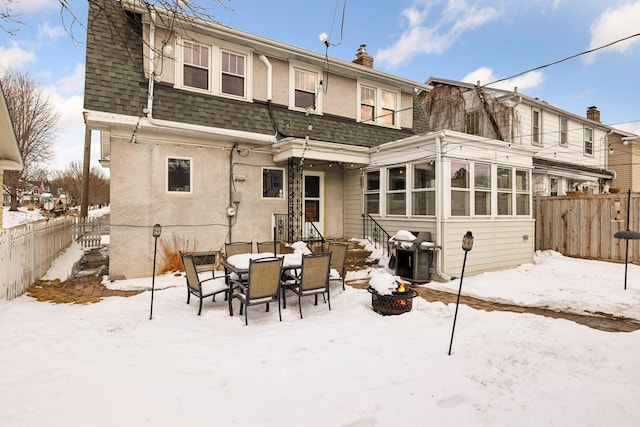 snow covered rear of property with mansard roof, roof with shingles, fence, and stucco siding