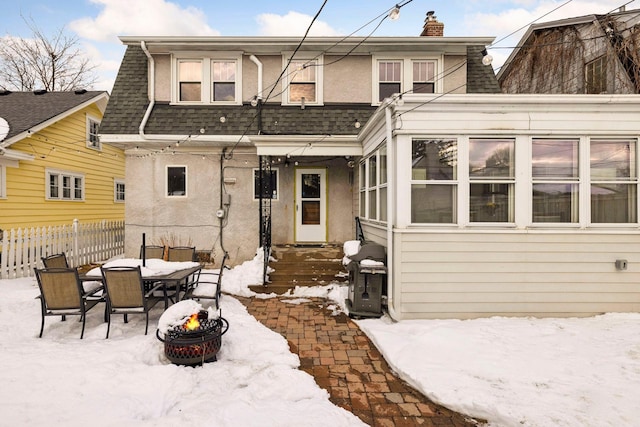 snow covered property with a shingled roof, fence, a fire pit, and stucco siding