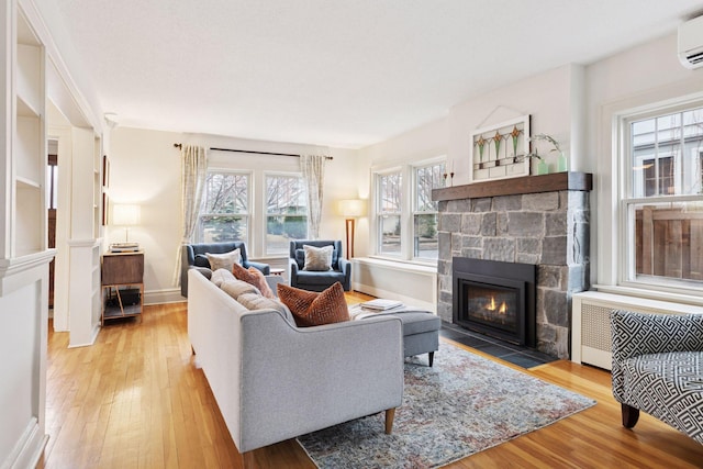 living room featuring a fireplace, wood finished floors, baseboards, a wall mounted AC, and radiator heating unit