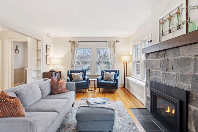 living area featuring built in shelves, a fireplace, baseboards, and wood finished floors