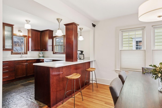 kitchen with reddish brown cabinets, pendant lighting, light countertops, and a sink