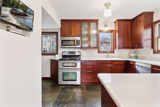 kitchen with stainless steel appliances, light countertops, glass insert cabinets, stone finish floor, and a sink