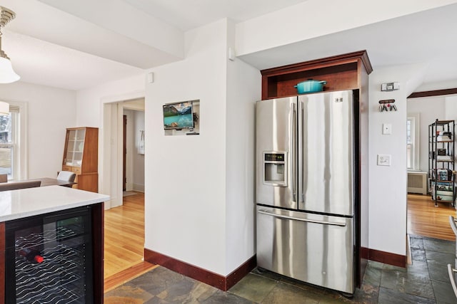 kitchen with stone tile flooring, beverage cooler, stainless steel refrigerator with ice dispenser, and baseboards