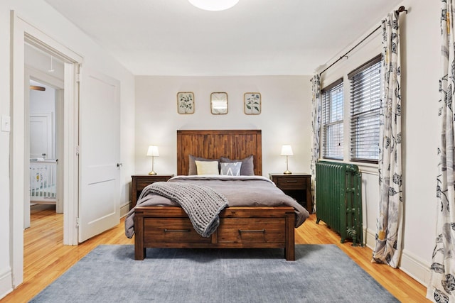 bedroom featuring light wood-type flooring, radiator heating unit, and baseboards