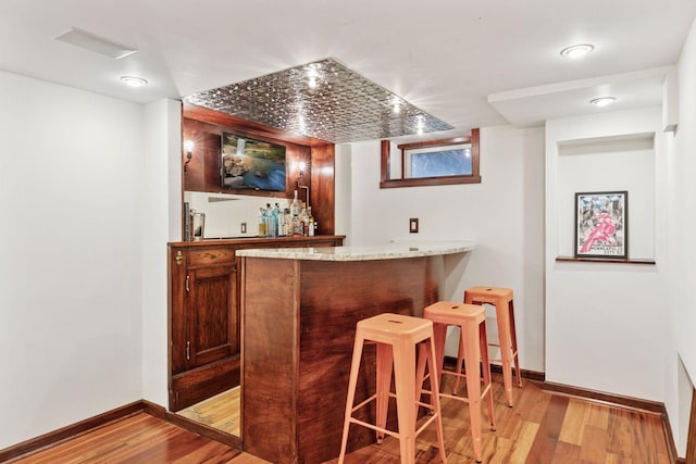 bar featuring a bar, light wood-style floors, and baseboards