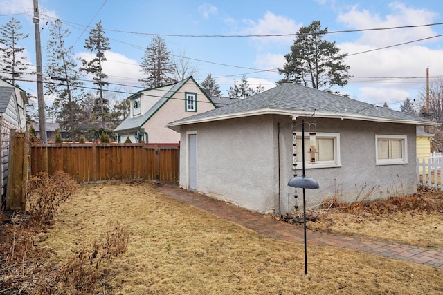 view of side of property featuring a shingled roof, a lawn, a fenced backyard, and stucco siding