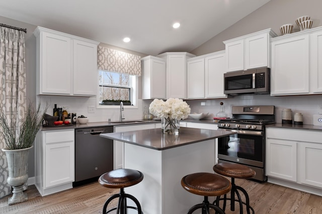 kitchen featuring appliances with stainless steel finishes, sink, a breakfast bar area, white cabinetry, and lofted ceiling