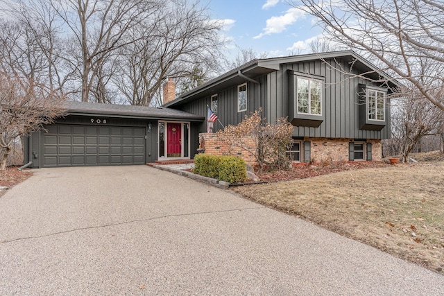 split level home with driveway, board and batten siding, an attached garage, brick siding, and a chimney