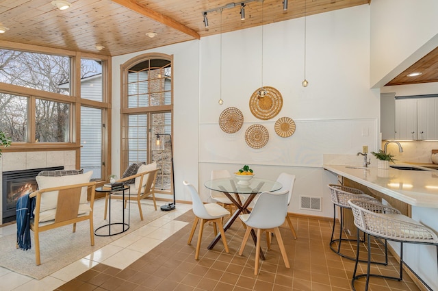 dining area with visible vents, a tiled fireplace, wooden ceiling, a high ceiling, and light tile patterned flooring