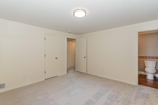 unfurnished bedroom with baseboards, ensuite bathroom, visible vents, and carpet flooring