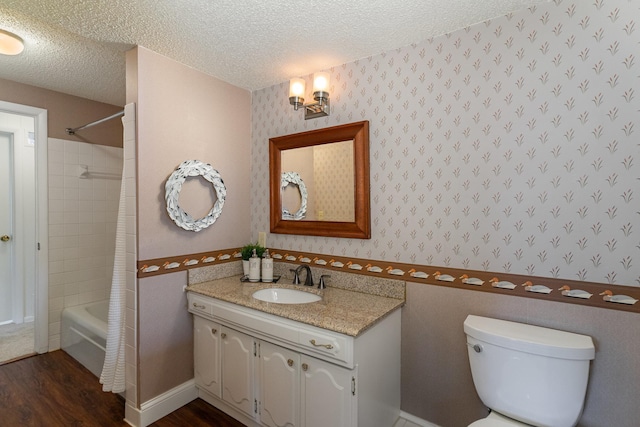 full bath with a textured ceiling, wallpapered walls, vanity, and wood finished floors