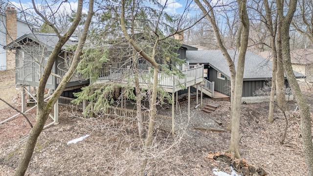 rear view of property with a chimney, roof with shingles, a deck, and stairs