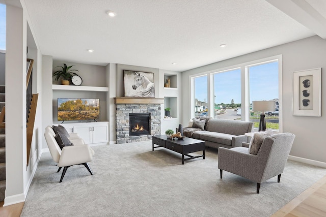 living room with a stone fireplace, built in features, a textured ceiling, and light wood-type flooring