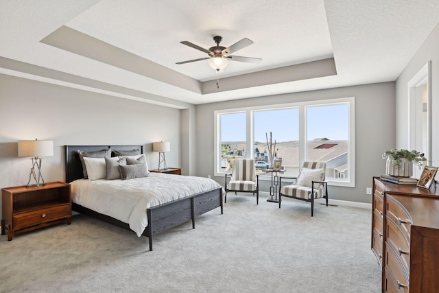 bedroom featuring a textured ceiling, light colored carpet, a raised ceiling, and ceiling fan