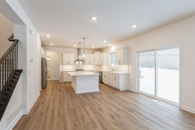 kitchen featuring appliances with stainless steel finishes, a kitchen island, white cabinets, and hanging light fixtures