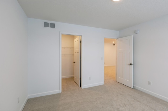 unfurnished bedroom with a spacious closet, a closet, and light carpet