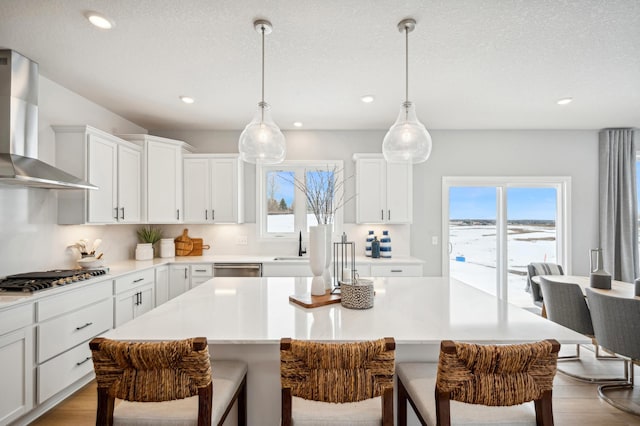 kitchen with decorative light fixtures, wall chimney range hood, a center island, white cabinetry, and appliances with stainless steel finishes