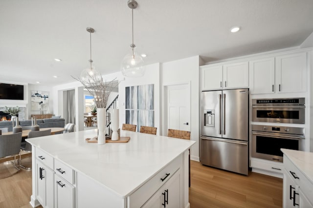 kitchen with white cabinetry, stainless steel appliances, a stone fireplace, and a kitchen island