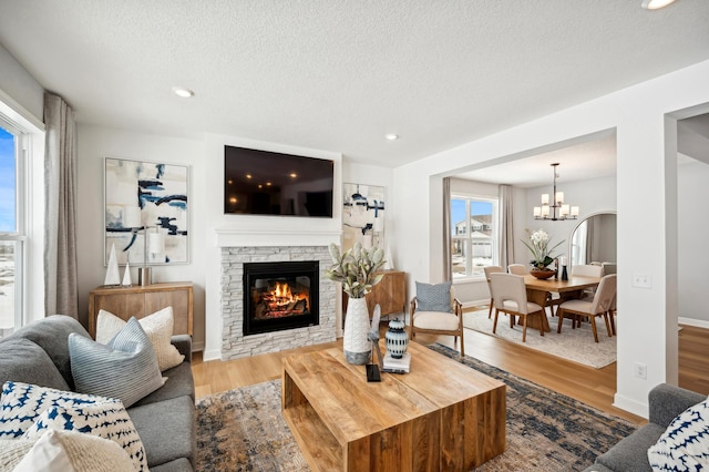 living room featuring light wood-type flooring, an inviting chandelier, a stone fireplace, and a textured ceiling