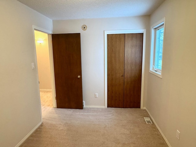 unfurnished bedroom with light carpet, a closet, and a textured ceiling