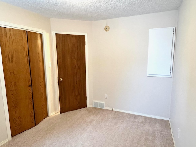 unfurnished bedroom featuring light colored carpet, a textured ceiling, and a closet