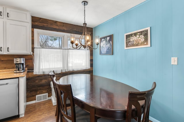 dining space with hardwood / wood-style floors, a notable chandelier, and wooden walls