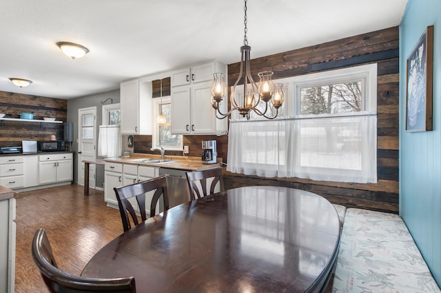 dining space with hardwood / wood-style floors, sink, wooden walls, and a chandelier