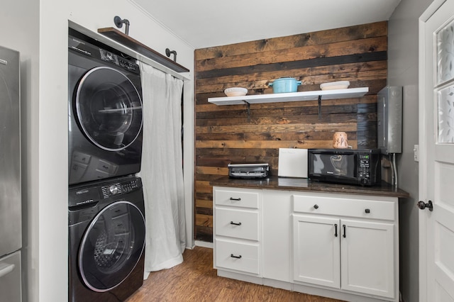 laundry area featuring light wood-type flooring, stacked washer and dryer, and wooden walls