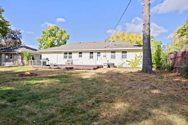 rear view of property with a fire pit, a deck, and a lawn