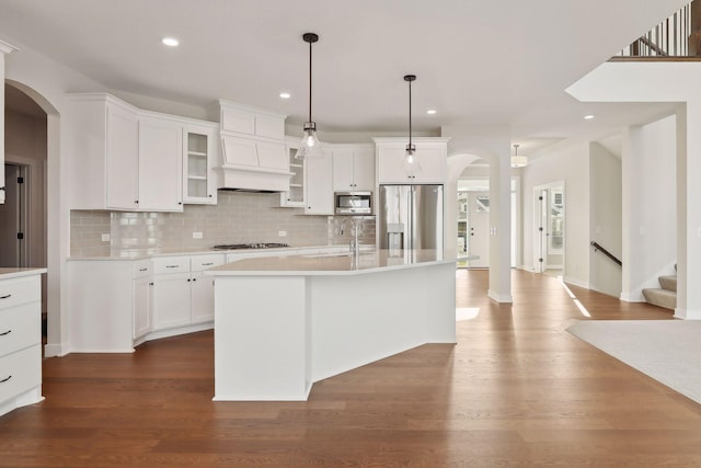 kitchen with a kitchen island with sink, dark wood-type flooring, hanging light fixtures, sink, and stainless steel appliances