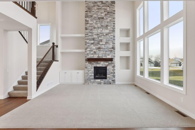 unfurnished living room featuring carpet flooring, built in shelves, a stone fireplace, and a high ceiling