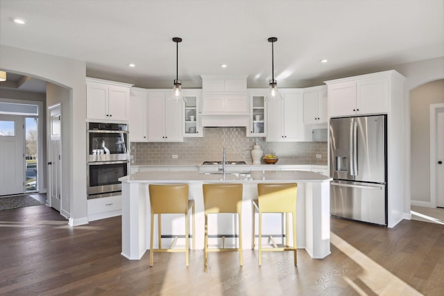 kitchen with dark hardwood / wood-style floors, an island with sink, stainless steel appliances, and decorative light fixtures