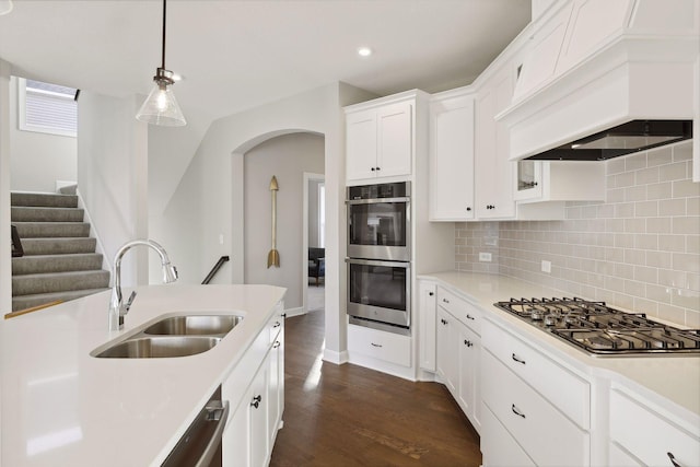 kitchen with appliances with stainless steel finishes, dark hardwood / wood-style flooring, premium range hood, sink, and white cabinets