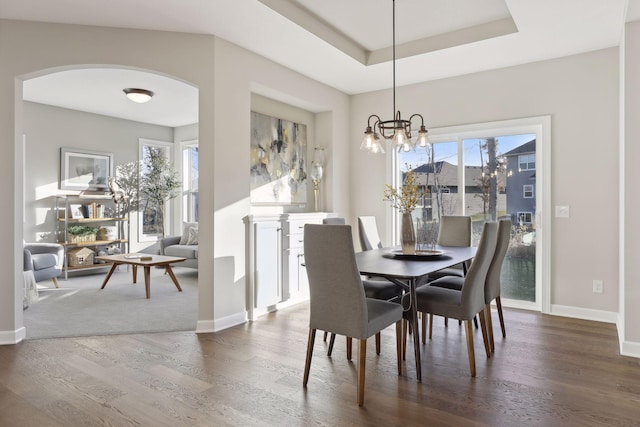 dining area with dark wood-type flooring, a tray ceiling, and a chandelier