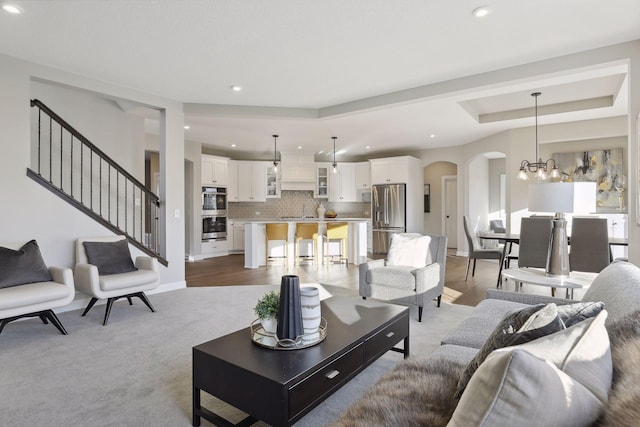 living room with light colored carpet, a raised ceiling, and a notable chandelier