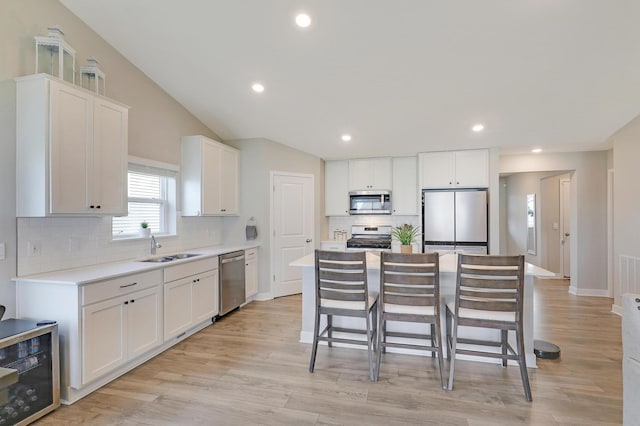 kitchen with stainless steel appliances, sink, vaulted ceiling, and white cabinets