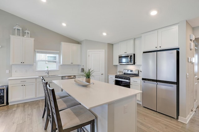 kitchen featuring lofted ceiling, appliances with stainless steel finishes, a kitchen island, white cabinets, and a kitchen bar