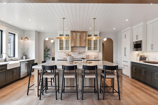 kitchen with appliances with stainless steel finishes, light stone counters, pendant lighting, light hardwood / wood-style flooring, and a center island