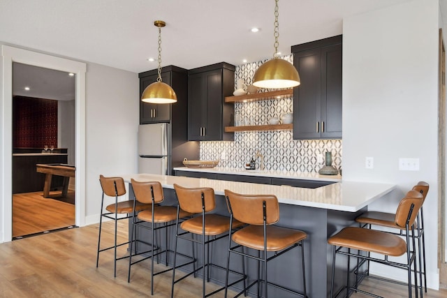 kitchen featuring kitchen peninsula, stainless steel fridge, light wood-type flooring, a breakfast bar, and hanging light fixtures