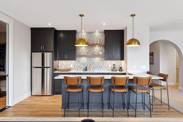 kitchen with decorative light fixtures, a kitchen breakfast bar, light wood-type flooring, and stainless steel refrigerator