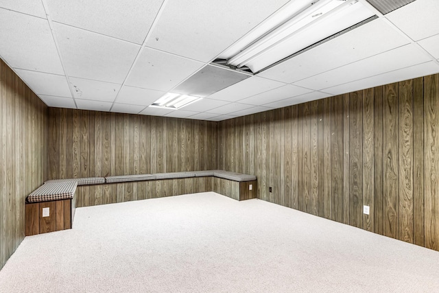 basement with a paneled ceiling, carpet floors, and wooden walls