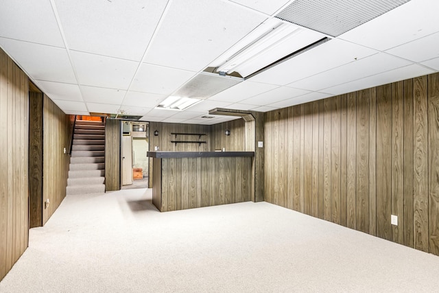 basement featuring a paneled ceiling, wood walls, carpet, and indoor bar