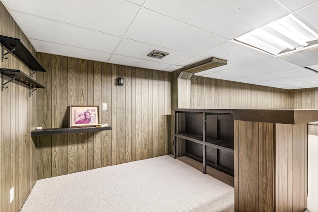 interior space with carpet floors, a drop ceiling, and wood walls