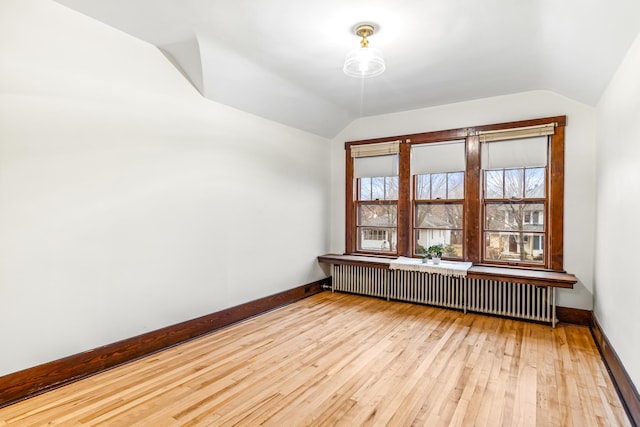 spare room featuring radiator heating unit, light hardwood / wood-style floors, and vaulted ceiling